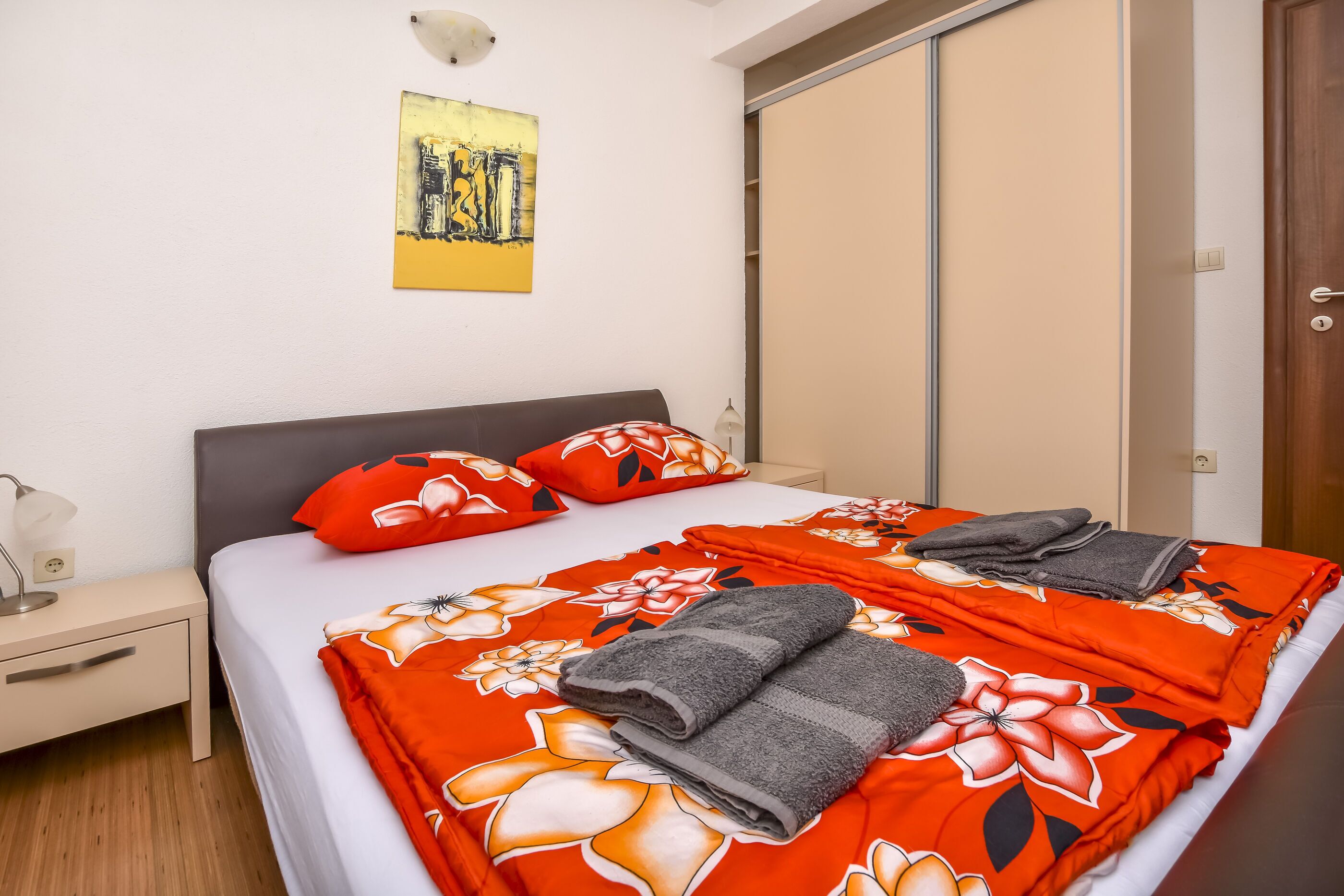 Ein ordentlich bezogenes Bett mit floralem Überwurf, zwei Kissen und gefalteten Handtüchern.