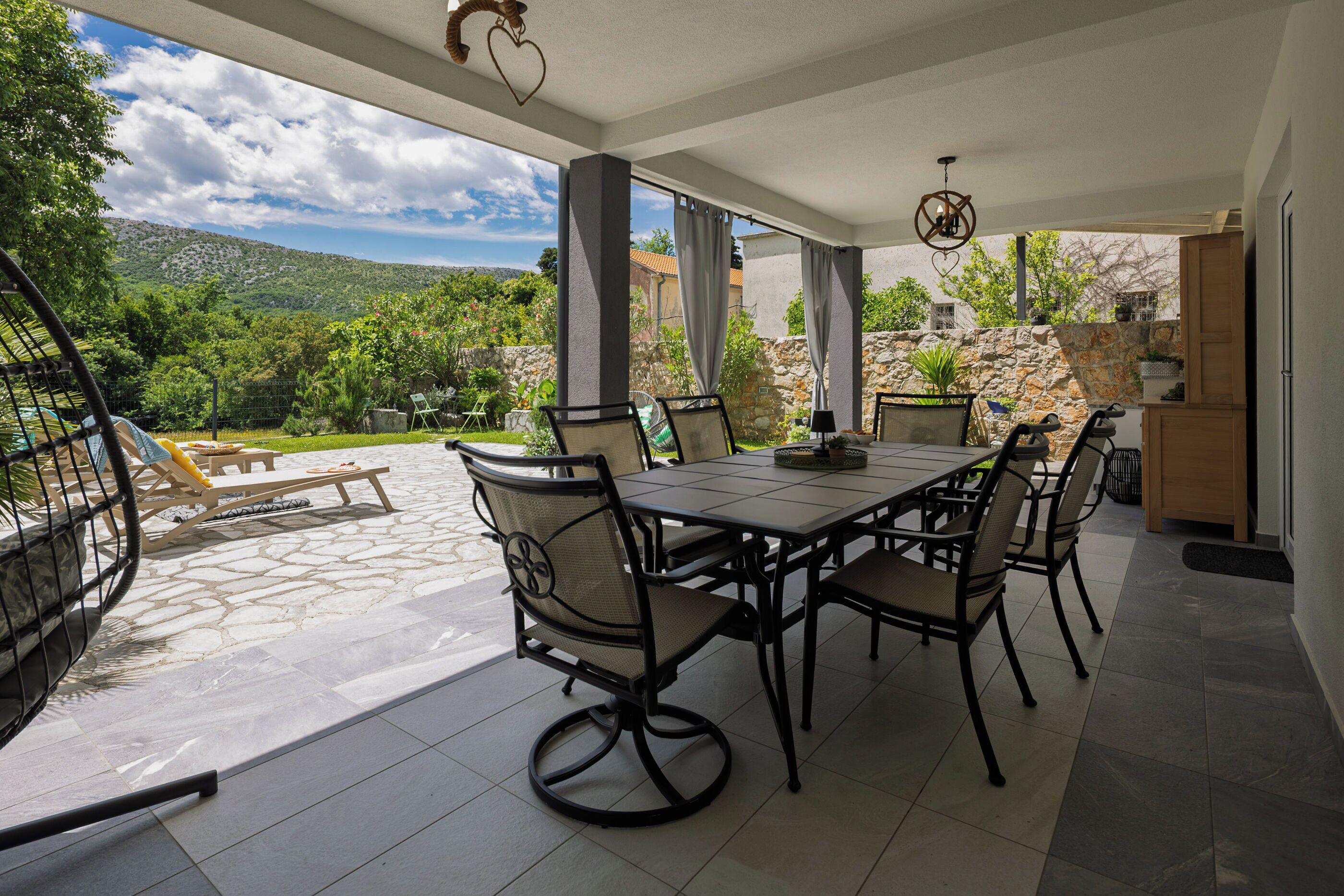 Un patio techado con una mesa y sillas de comedor, una lámpara colgante y vistas del paisaje circundante.