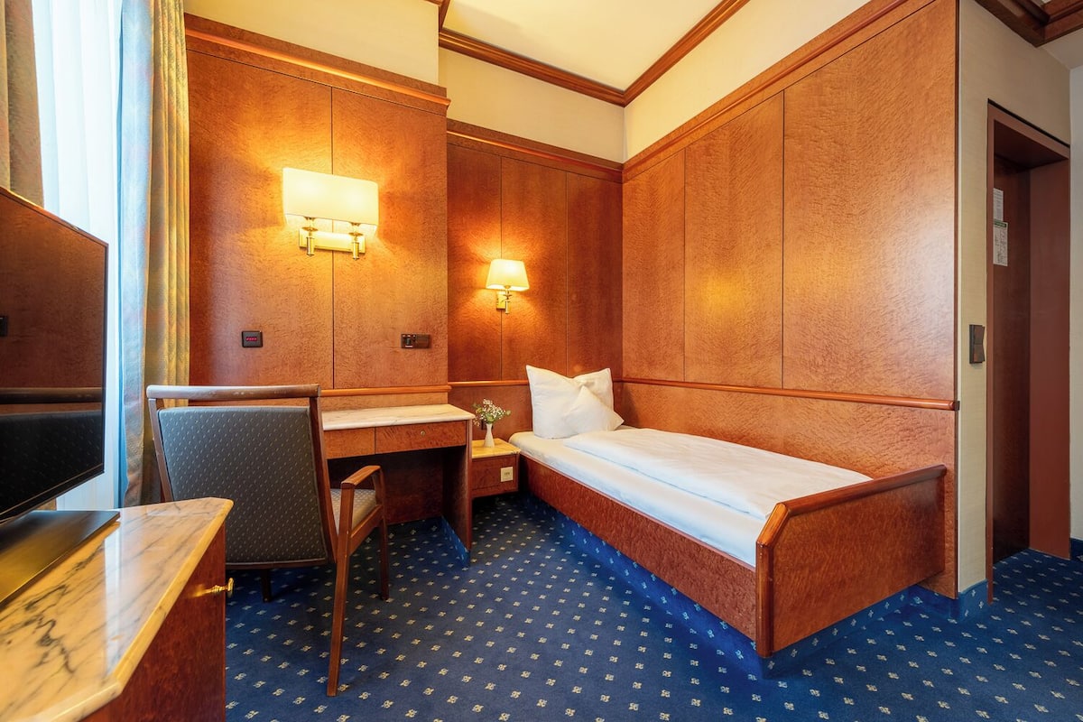 A hotel room with a bed, desk, chair, and two wall-mounted lamps.