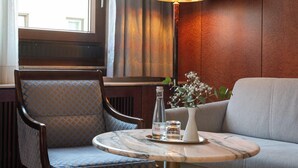 Et hotelværelse med et rundt bord, en sofa, en stol, en lampe og et vindue med gardiner.