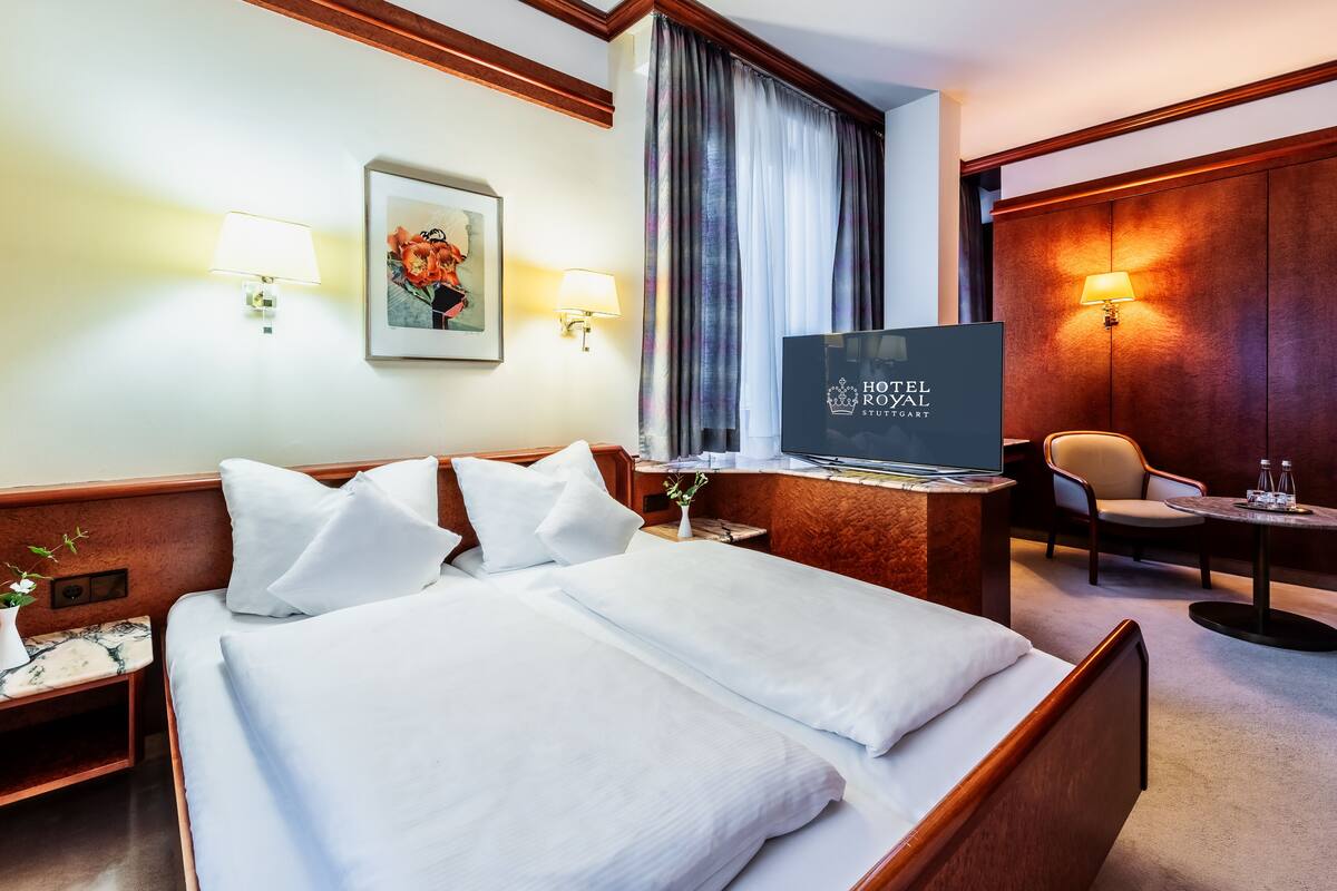 A hotel room with a large bed, a desk with a TV, a chair, and a small table with a lamp.