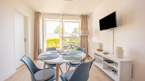 Un espace repas moderne avec une table ronde, six chaises, un téléviseur fixé au mur et une console blanche agrémentée d’une lampe et d’objets décoratifs.