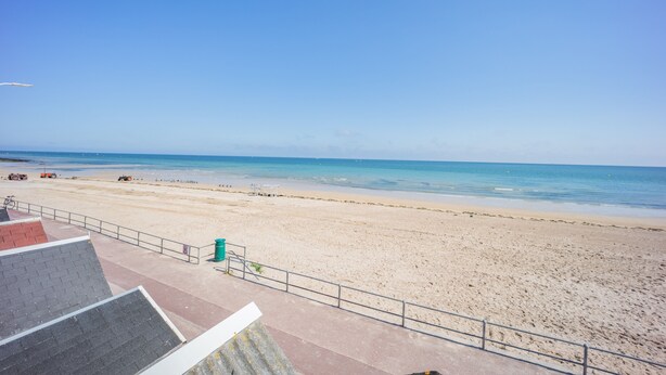 Une plage avec un ciel dégagé, un rivage sablonneux et une promenade dallée qui mène à l’eau.