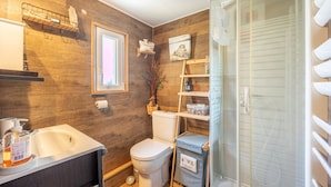 A bathroom with a wooden wall, a sink, a toilet, a shower, and a small shelf with toiletries.