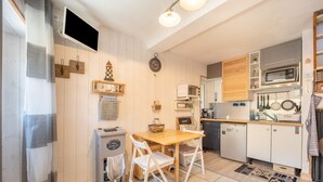 A compact kitchen with wooden cabinets, a microwave, and a sink. There is a wooden dining table with chairs and a small island with a basket.
