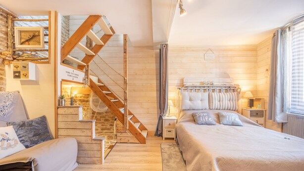 A cozy bedroom with a wooden staircase, a bed with striped bedding, and a nightstand with a lamp.
