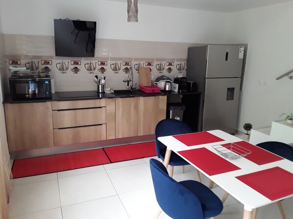 A compact kitchen with wooden cabinets, a microwave, a sink, and a refrigerator. There is a dining area with a table and chairs.