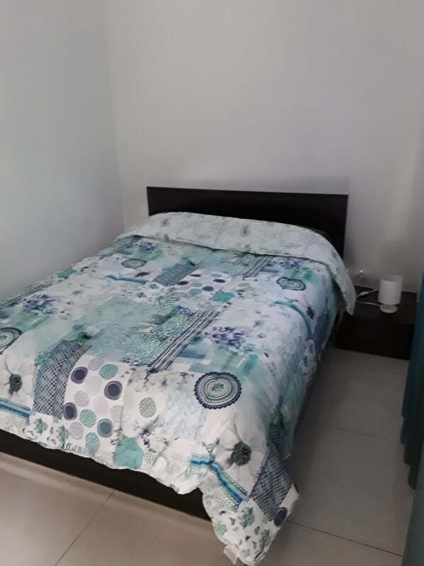 A bed with a patterned bedspread, a black headboard, and a bedside table with a lamp. - Les creolia 2 (Le Tampon)