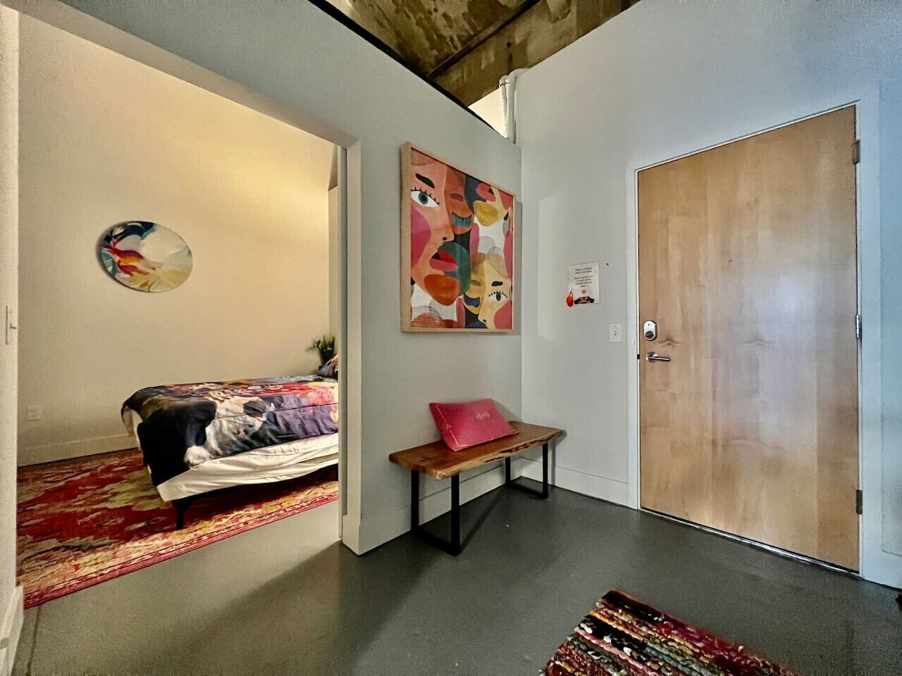 Una habitación con una cama, un banco, una puerta y una pared decorada con arte abstracto.