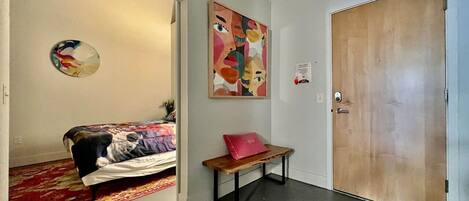 Una habitación con una cama, un banco, una puerta y una pared decorada con arte abstracto.