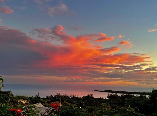A coastal landscape with a sunset, featuring a view of the sea and a distant island.