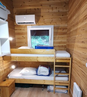 Una cabaña de madera pequeña con literas, televisor y aire acondicionado integrado.