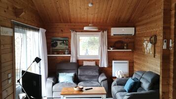 Een gezellig chaletinterieur met een plafondventilator, houten wanden, een grijze bank, een houten salontafel en een televisie.