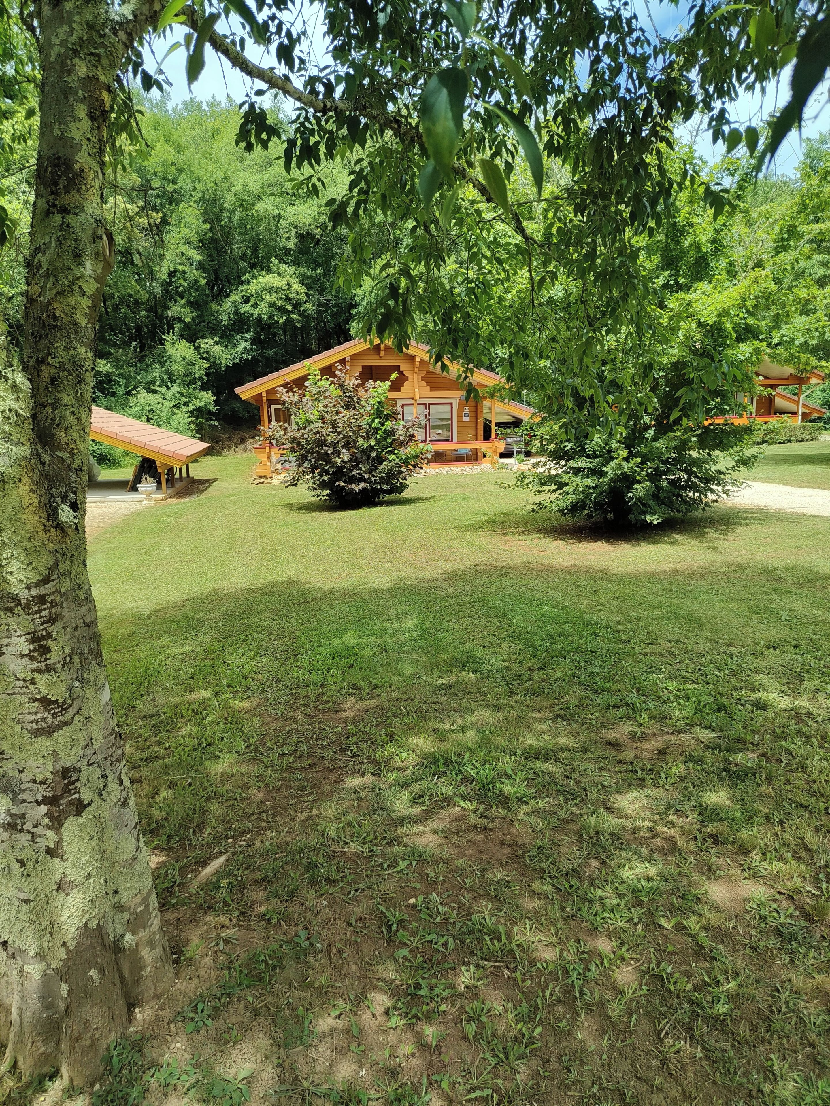 Une cabane en bois avec un toit rouge, entourée d’une pelouse bien entretenue et d’arbres.