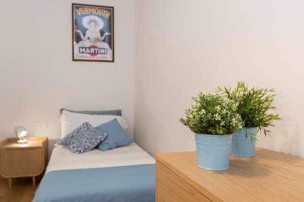 Une chambre à coucher avec un lit, une table de chevet, une affiche murale et deux plantes en pot.