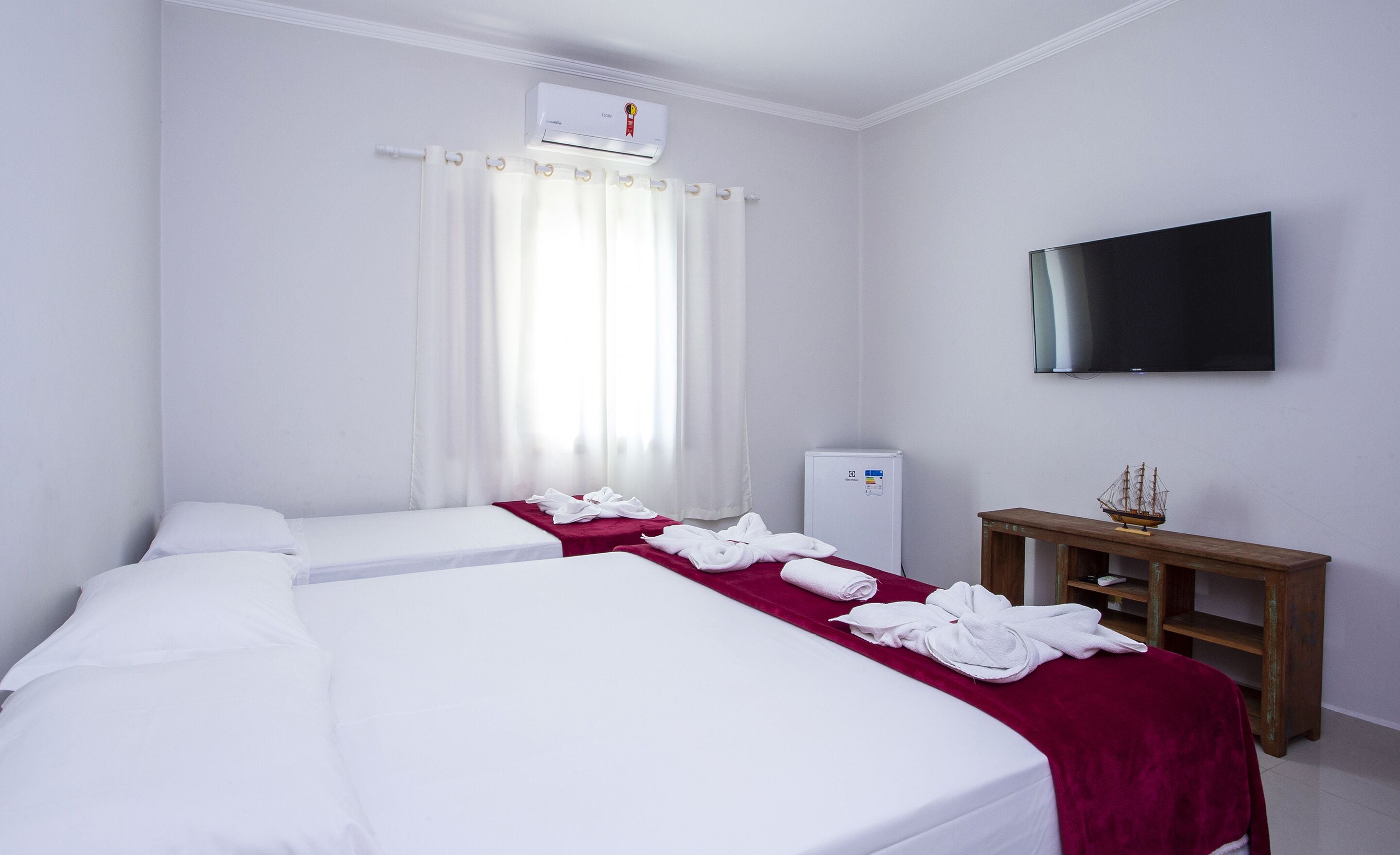 A hotel room with two beds, a flat-screen TV, a minibar, and a window with curtains.