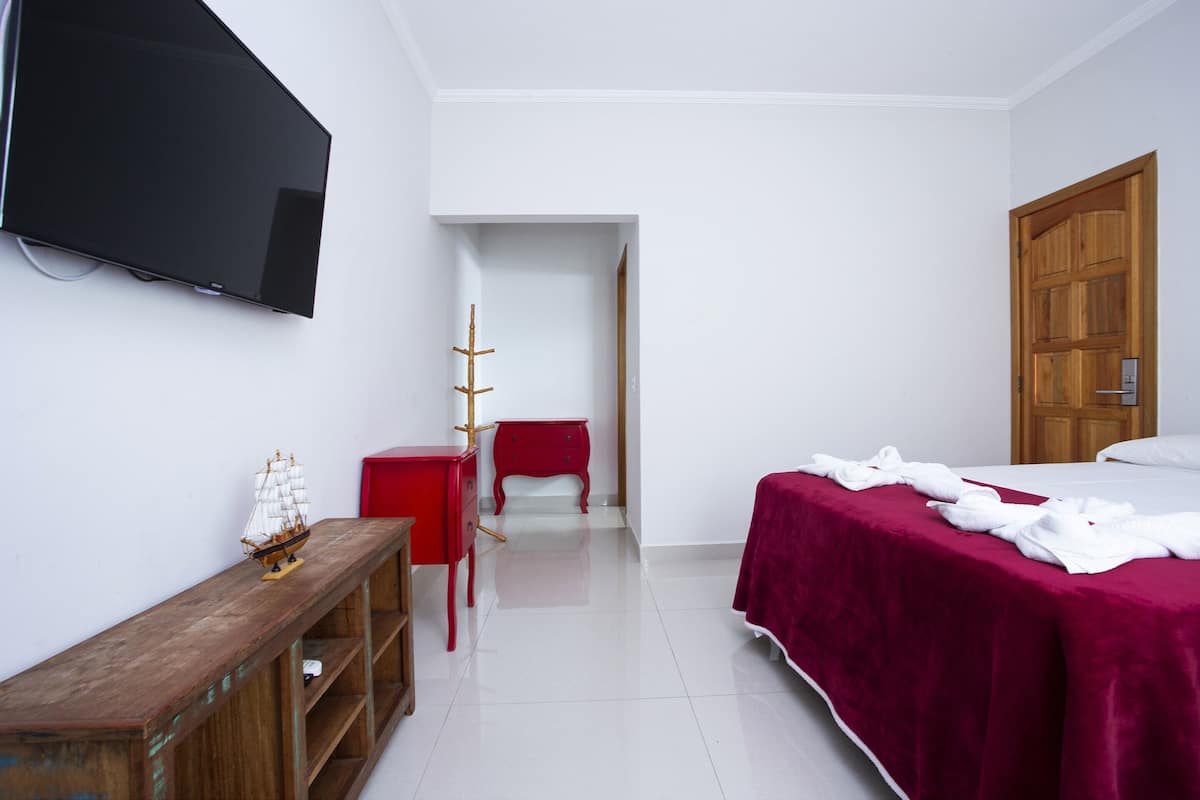 Una habitación de hotel con cama, televisión, cómoda de madera, una silla roja y una puerta.