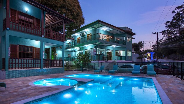 A hotel with a swimming pool, multiple balconies, and a well-lit exterior. - Pousada Guarubela Veloso (Ilhabela)