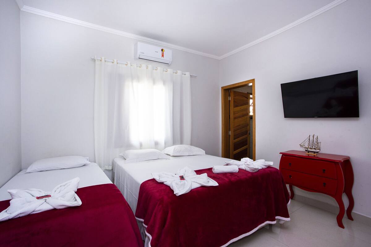 Habitación de hotel con dos camas, un televisor, un aparador rojo y un equipo de aire acondicionado.