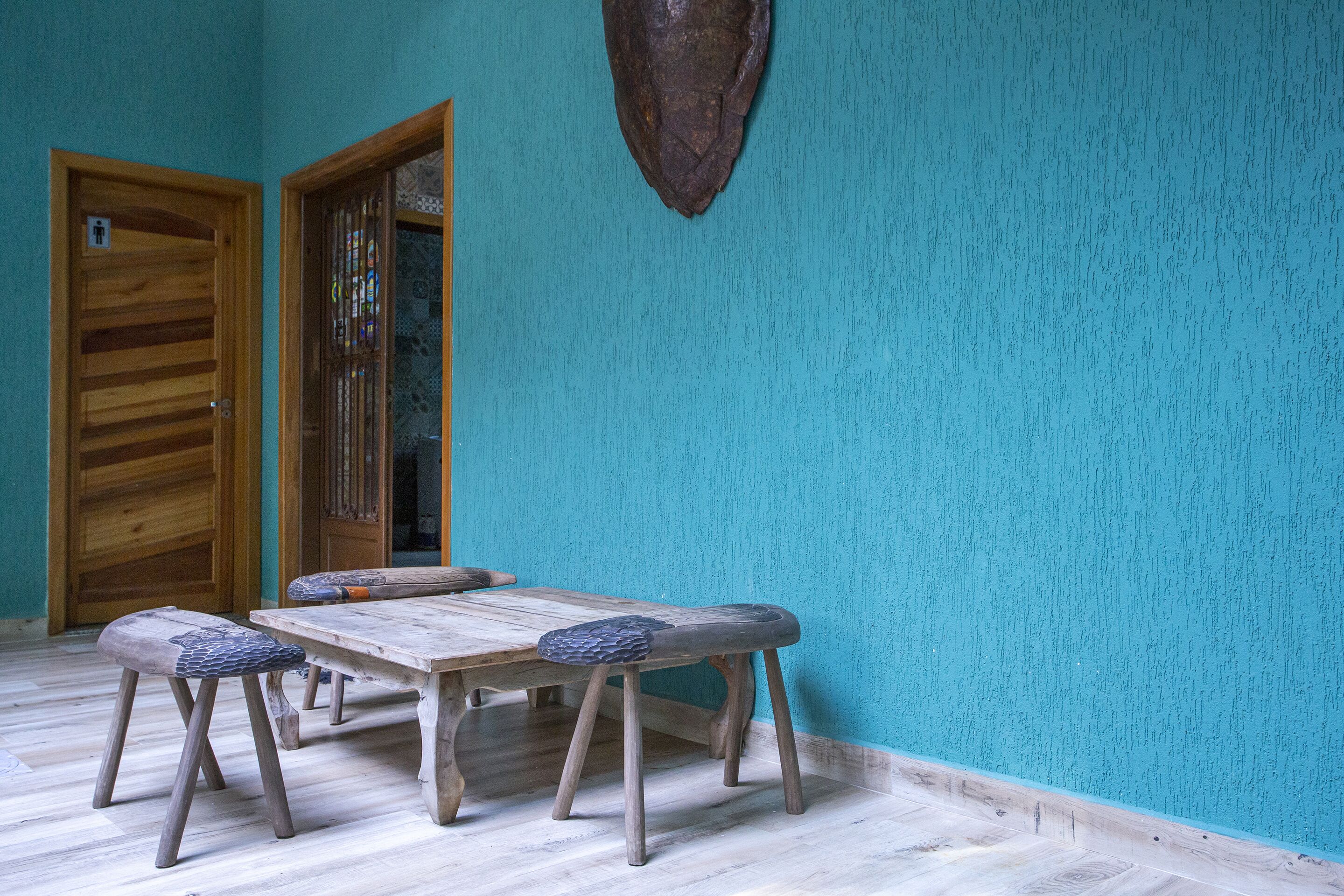 A room with a wooden table and benches, a wooden door, and a textured teal wall.