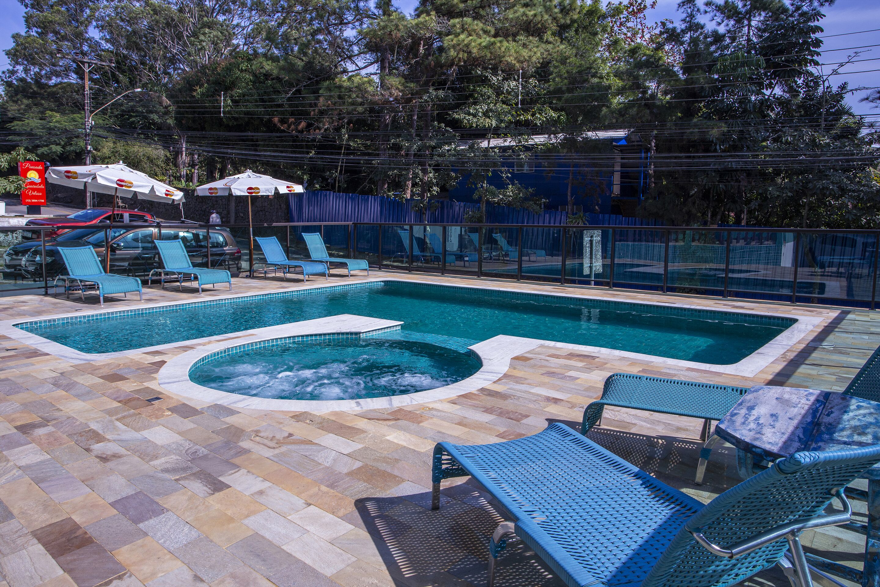 A swimming pool with lounge chairs and umbrellas, surrounded by a fence and trees.