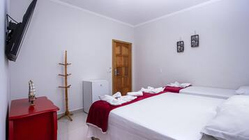 Quarto de hotel com cama, televisão presa na parede, cabideiro e pequeno frigorífico.