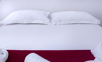Una cama con ropa de cama blanca y una manta roja.