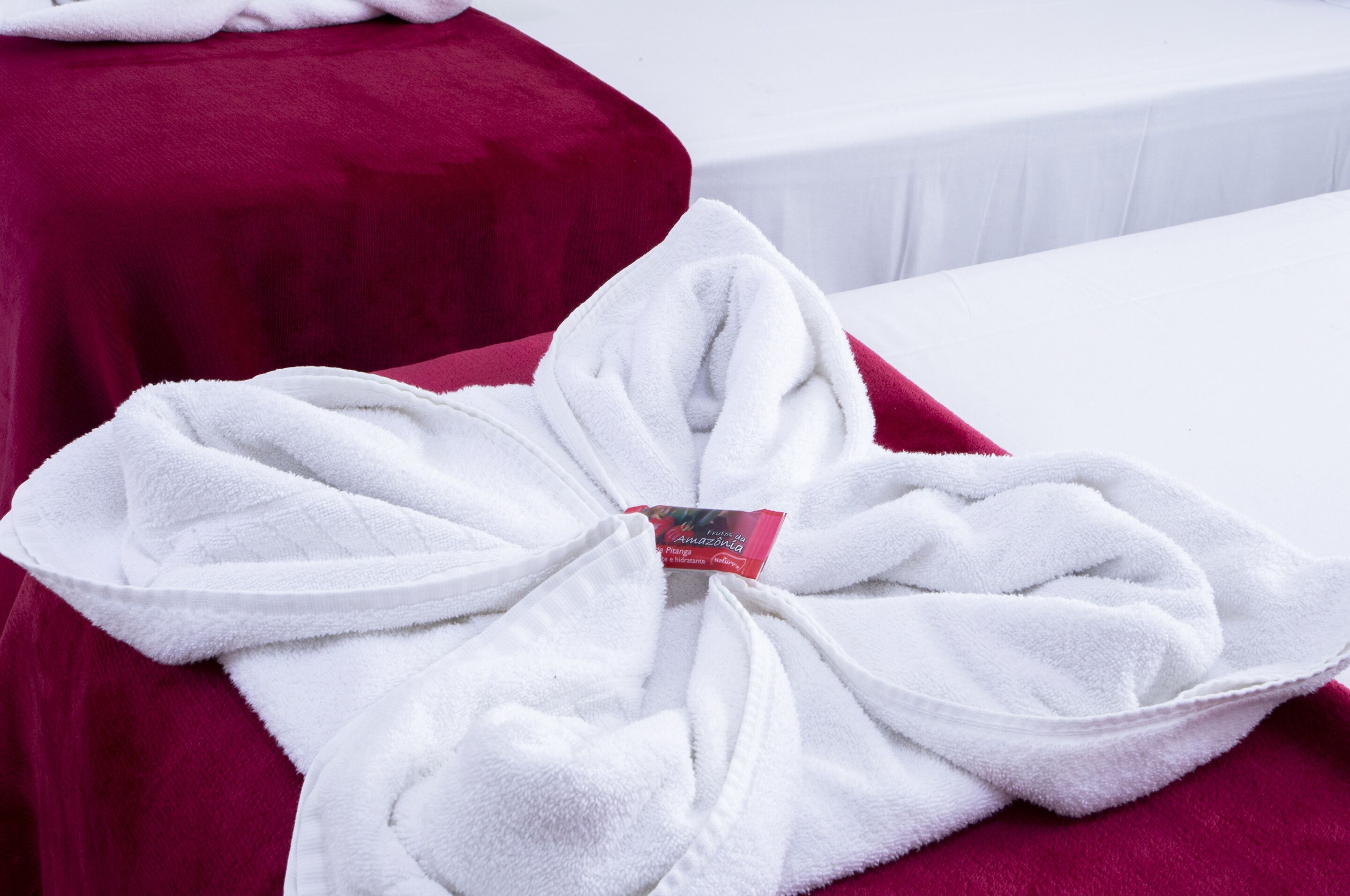 Un accappatoio bianco annodato a fiocco su un letto con una coperta rossa.
