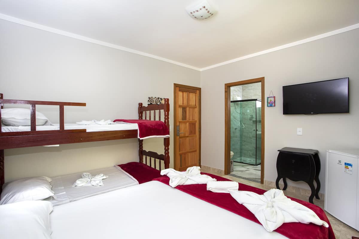 Una habitación de hotel con literas, una cama individual, un televisor, un mueble pequeño y una puerta que da al baño.