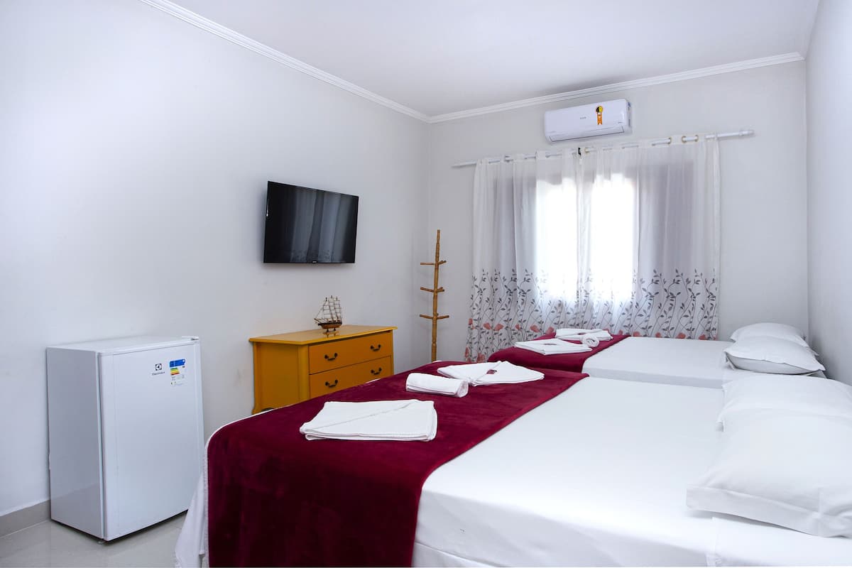 Habitación de hotel con cama, televisión, refrigerador pequeño y ventana con cortinas.