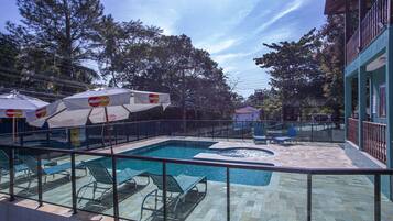 Un espace piscine aménagé avec des chaises longues et des parasols, entouré d’une clôture et d’arbres.