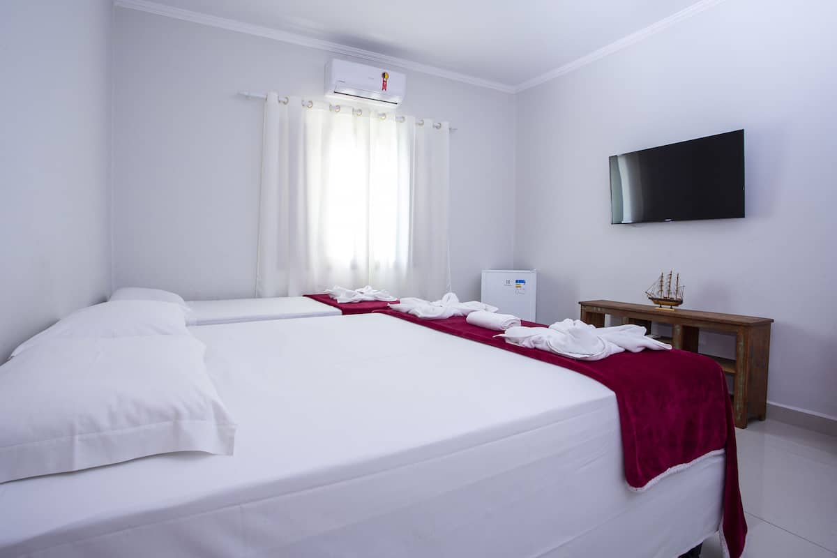 Habitación de hotel con una cama grande, un televisor de pantalla plana en la pared, una mesita con un modelo de barco y una ventana con cortinas.