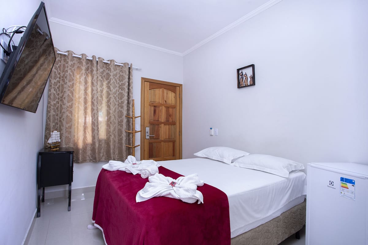 Habitación de hotel con una cama, un televisor montado en la pared, una puerta de madera y una pequeña mesa con un modelo de barco.