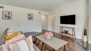 Un salón moderno con un sofá gris, una mesa de centro y un televisor de pantalla plana sobre un mueble de madera.