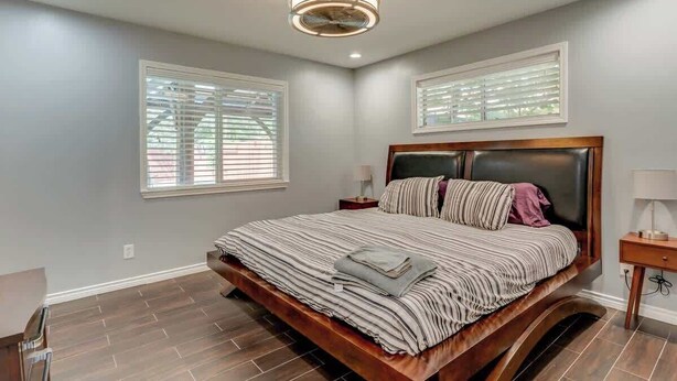 Un dormitorio con una cama grande, un ventilador de techo y dos ventanas con persianas.