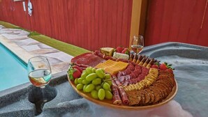 Una tabla de fiambres con diferentes carnes, quesos y frutas junto a una piscina.