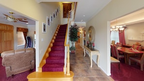 A staircase with a red carpet, wooden walls, a dining area with a chandelier, and a ceiling fan. - East Wing - Exquisite Mountain Estate with Pool (Silver City)