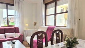 Una habitación con una mesa de comedor, sillas, un sofá y un ventanal con cortinas.