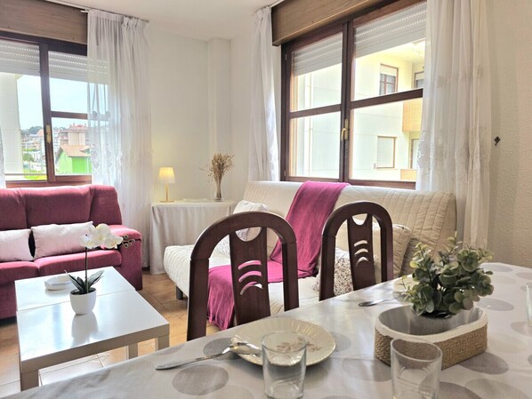 Une pièce comprenant une table à manger, des chaises, un canapé et une fenêtre avec des rideaux.