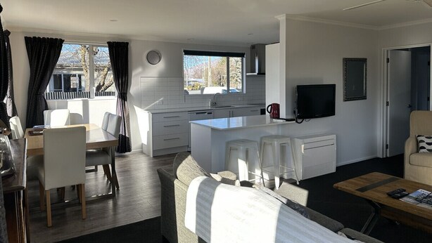 Een moderne, goed verlichte woonkamer met een eethoek, een keuken met een centraal eiland, en een aan de muur bevestigde televisie.