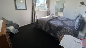 Een slaapkamer met een bed, een bureau, een stoel, een spiegel en een raam met gordijnen.