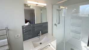 Een moderne badkamer met een witte wastafel, een grote spiegel en een douchecabine met glazen wanden.