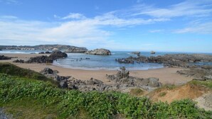 Paesaggio costiero con scogliere rocciose, una spiaggia sabbiosa e un cielo azzurro limpido.