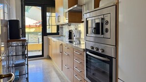 Una cucina compatta con elettrodomestici in acciaio inossidabile, mobili impiallacciati in legno e una porta a vetri scorrevoli che dà su uno spazio all'aperto.