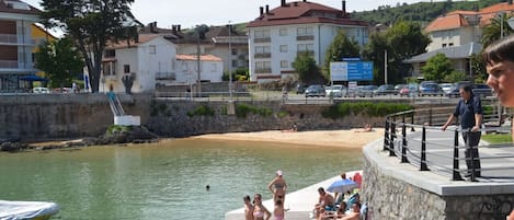 Una zona frente al agua con un muelle, gente cerca de la orilla y edificios al fondo.