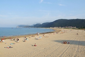 Uma extensa praia de areia com pessoas se banhando e nadando.