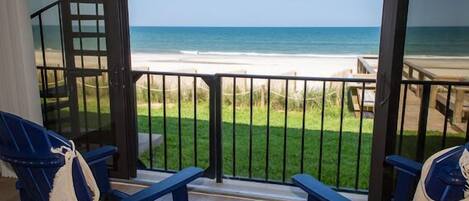 A balcony with a view of the beach, featuring two blue chairs and a small round table.