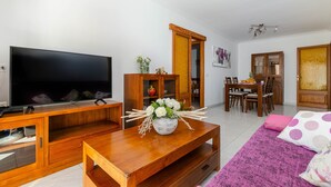 Un salon moderne doté d’un téléviseur à écran plat, de meubles en bois, d’un coin repas et d’un espace salon confortable agrémenté d’un tapis rose.