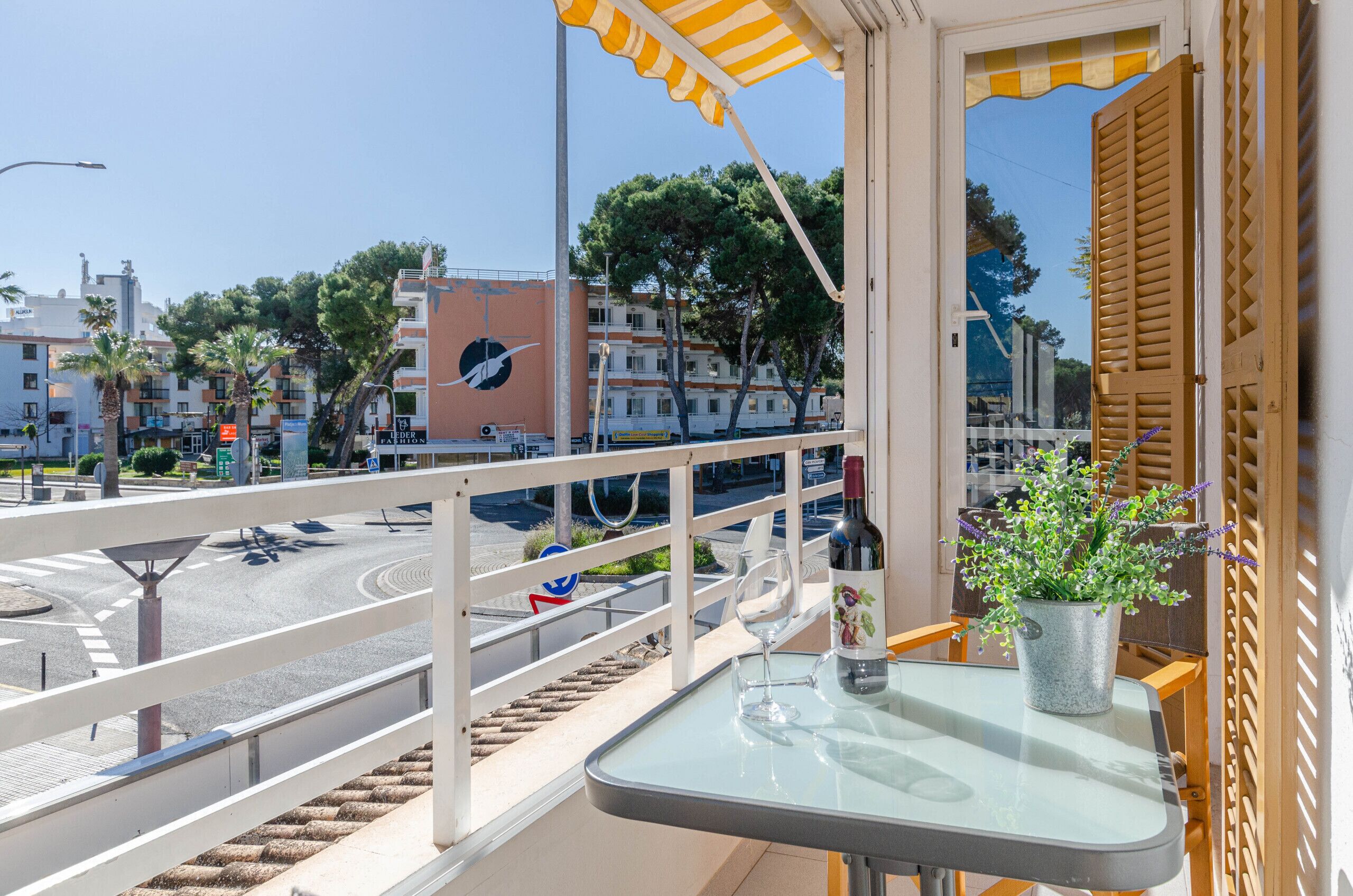 A balcony with a glass table, a wine bottle, and a potted plant.