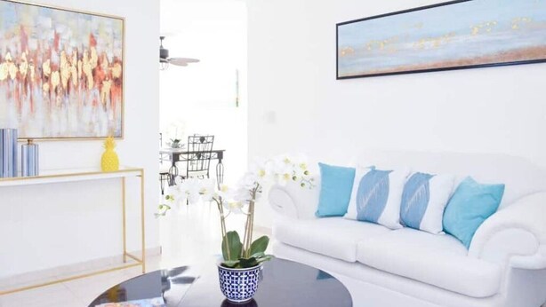 Een moderne woonkamer met een witte bank, een bijzettafeltje en een schilderij aan de muur.